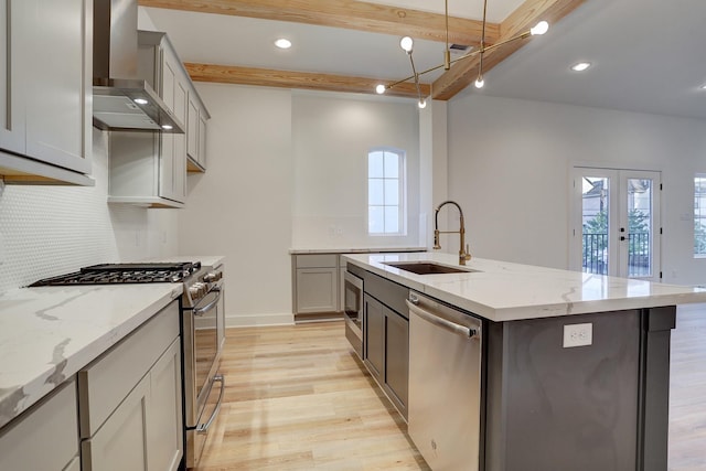 kitchen with wall chimney exhaust hood, sink, appliances with stainless steel finishes, gray cabinets, and an island with sink