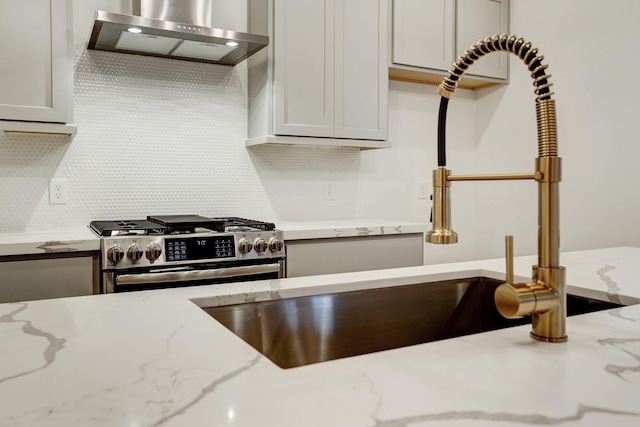 kitchen featuring wall chimney exhaust hood, stainless steel range with gas cooktop, light stone countertops, and backsplash