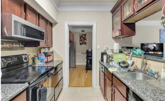 kitchen with a sink, stainless steel microwave, light stone counters, black range with electric cooktop, and glass insert cabinets