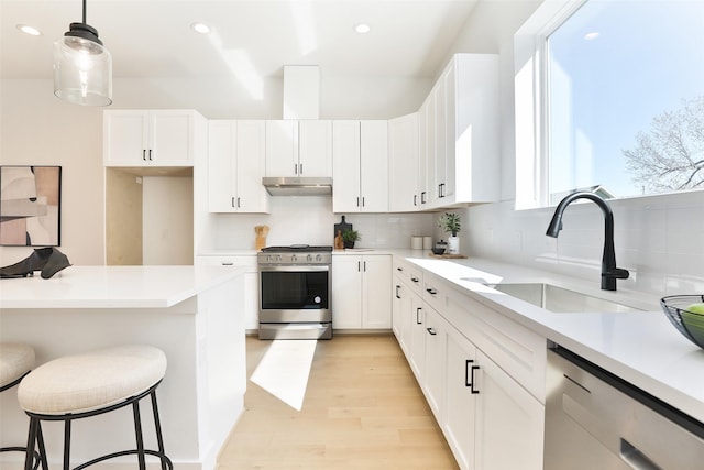 kitchen with a breakfast bar area, appliances with stainless steel finishes, a sink, white cabinetry, and backsplash