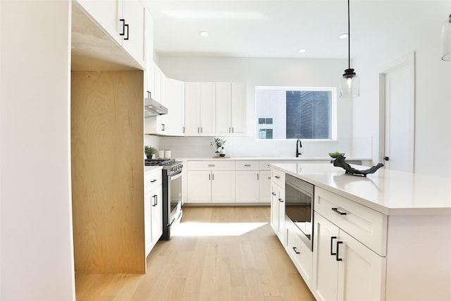 kitchen with light wood finished floors, stainless steel appliances, light countertops, white cabinets, and under cabinet range hood