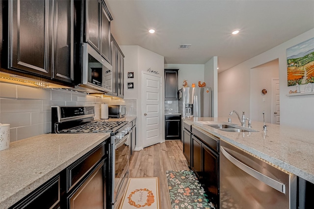 kitchen featuring appliances with stainless steel finishes, sink, backsplash, light stone countertops, and light wood-type flooring