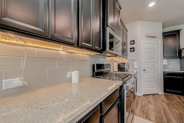 kitchen with appliances with stainless steel finishes, dark brown cabinetry, light stone counters, decorative backsplash, and light wood-type flooring