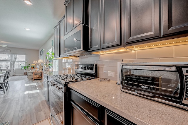 kitchen with tasteful backsplash, light stone countertops, light hardwood / wood-style floors, and appliances with stainless steel finishes