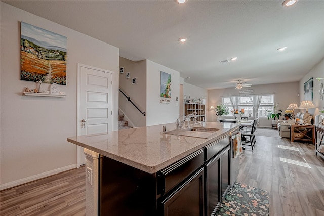 kitchen featuring an island with sink, sink, ceiling fan, light stone counters, and light hardwood / wood-style floors