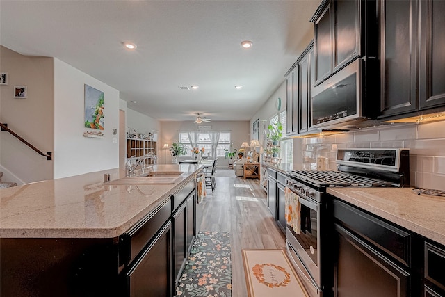 kitchen featuring an island with sink, sink, decorative backsplash, stainless steel appliances, and light stone countertops