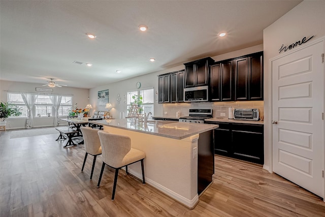 kitchen with a breakfast bar, stove, tasteful backsplash, an island with sink, and light wood-type flooring