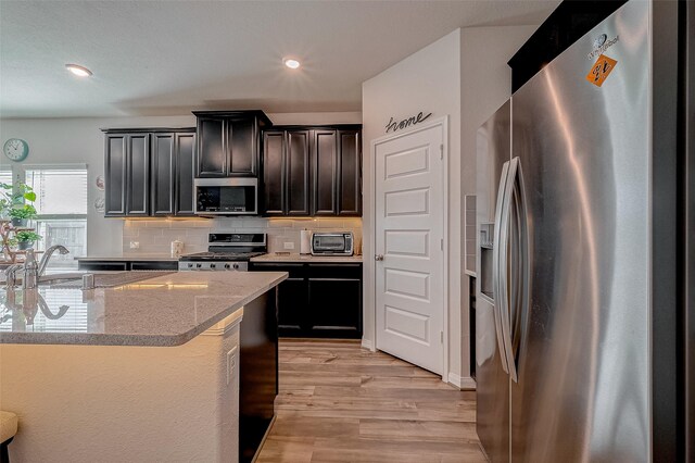 kitchen with sink, light hardwood / wood-style flooring, backsplash, stainless steel appliances, and light stone countertops