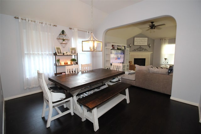 dining area featuring dark wood-type flooring, ceiling fan, lofted ceiling, and a tile fireplace