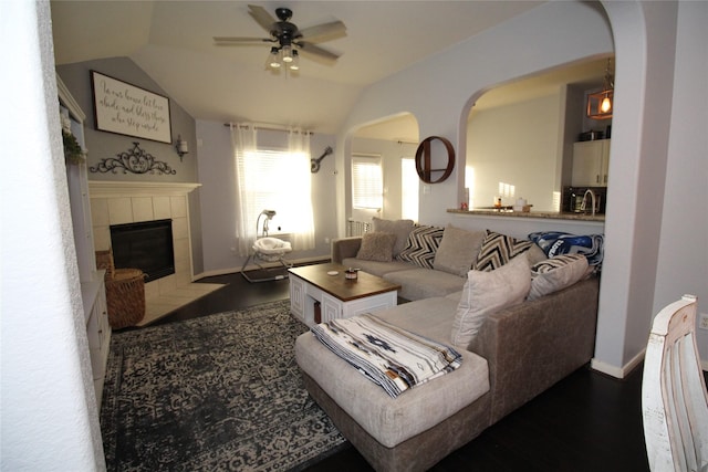 living room featuring a tile fireplace, lofted ceiling, dark wood-type flooring, and ceiling fan