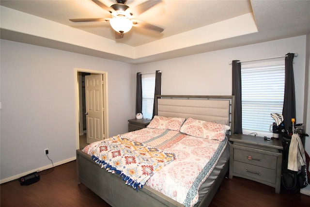 bedroom with dark wood-type flooring, ceiling fan, and a tray ceiling