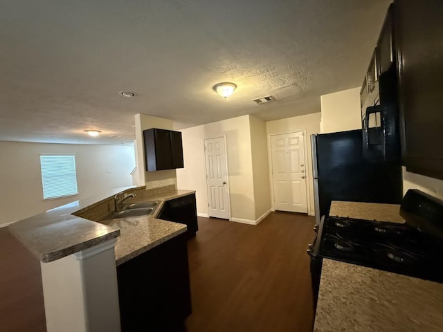 kitchen with sink, a textured ceiling, dark hardwood / wood-style flooring, kitchen peninsula, and black appliances