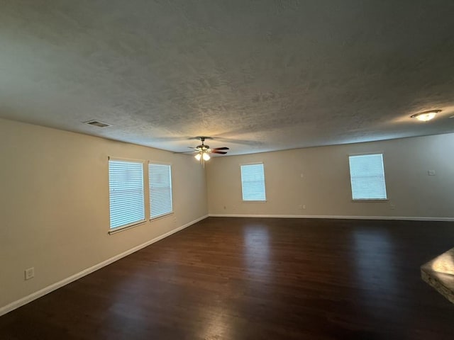 empty room with ceiling fan, a wealth of natural light, a textured ceiling, and dark hardwood / wood-style flooring