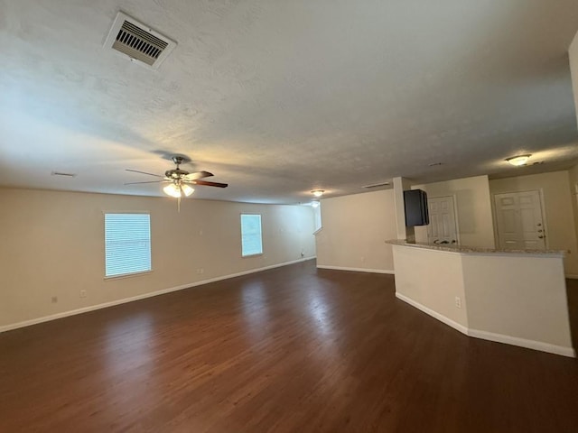 unfurnished living room featuring ceiling fan, dark wood-type flooring, and a textured ceiling