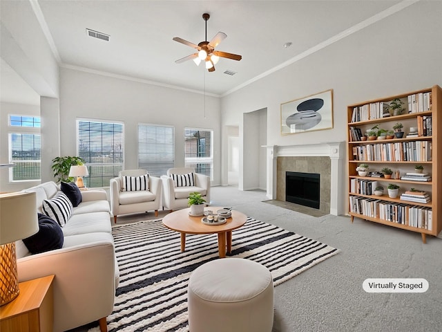 carpeted living room with ornamental molding, a tile fireplace, ceiling fan, and a high ceiling