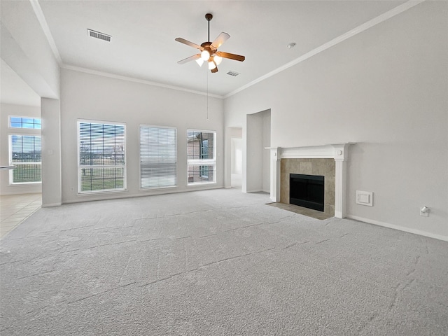 unfurnished living room featuring a tile fireplace, a high ceiling, ornamental molding, ceiling fan, and light carpet