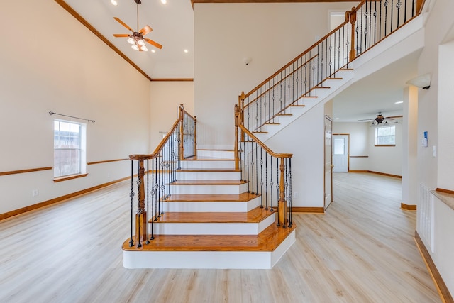 stairs with ceiling fan, a healthy amount of sunlight, hardwood / wood-style floors, and a high ceiling