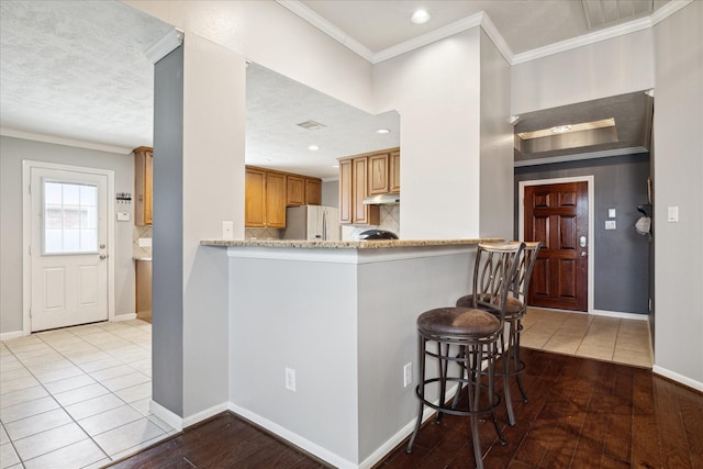 kitchen featuring a breakfast bar, stainless steel fridge, kitchen peninsula, crown molding, and light wood-type flooring