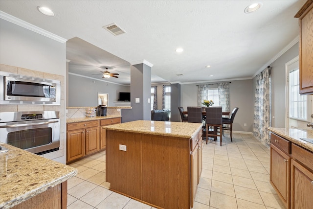 kitchen with light stone counters, crown molding, a center island, light tile patterned floors, and appliances with stainless steel finishes