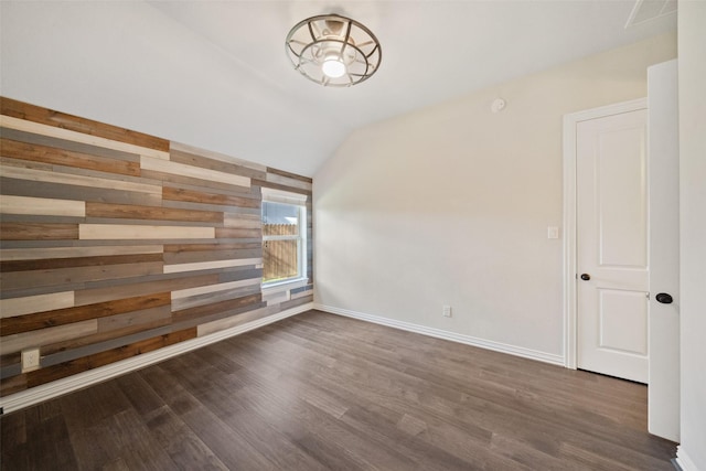 empty room featuring lofted ceiling, dark hardwood / wood-style flooring, and wood walls