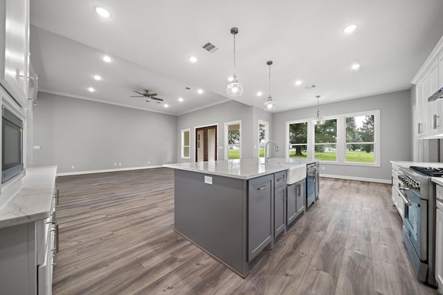 kitchen with a large island with sink, gray cabinetry, stainless steel appliances, white cabinets, and decorative light fixtures