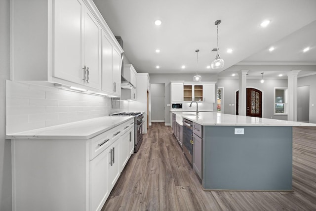 kitchen with a spacious island, white cabinets, hanging light fixtures, appliances with stainless steel finishes, and ornate columns