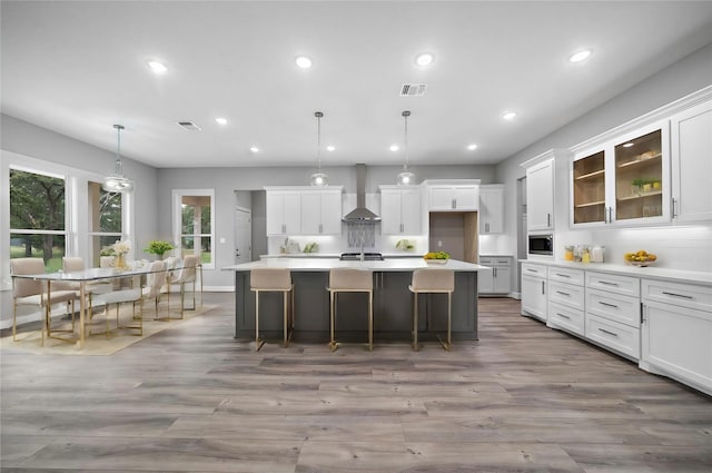 kitchen with white cabinetry, light countertops, wall chimney exhaust hood, stainless steel microwave, and decorative light fixtures