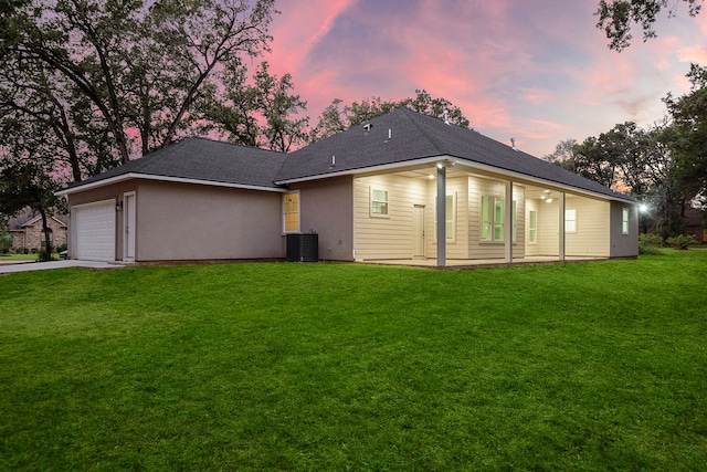 back of property featuring a garage, central AC, a lawn, and driveway