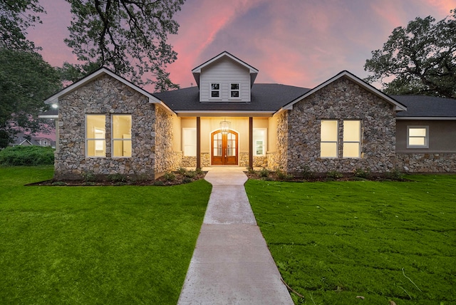 view of front of property with stucco siding, stone siding, a lawn, and french doors