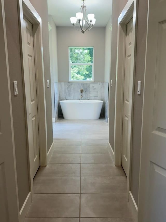 full bath with a chandelier, a soaking tub, and tile patterned flooring