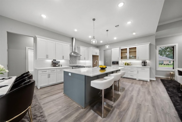 kitchen featuring pendant lighting, light countertops, wall chimney range hood, and white cabinets