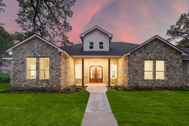 view of front of home with stucco siding, a shingled roof, a lawn, and french doors