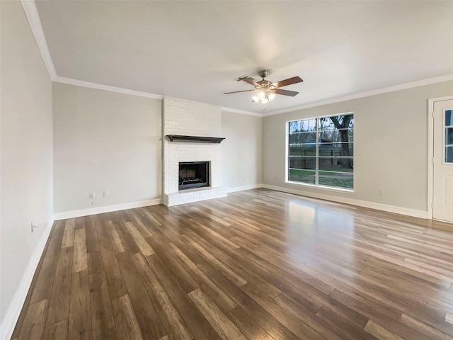 unfurnished living room with a brick fireplace, dark wood-type flooring, ornamental molding, and ceiling fan