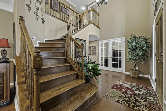 stairway featuring ornamental molding, a towering ceiling, hardwood / wood-style floors, and french doors