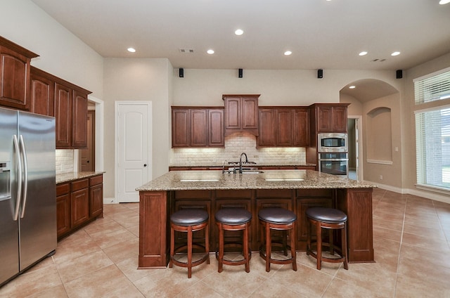 kitchen featuring sink, a kitchen island with sink, stainless steel appliances, a kitchen breakfast bar, and tasteful backsplash