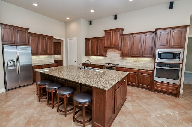 kitchen featuring appliances with stainless steel finishes, sink, a breakfast bar area, a kitchen island with sink, and light stone counters