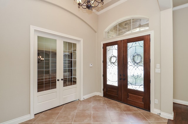 foyer with ornamental molding, light tile patterned floors, an inviting chandelier, and french doors