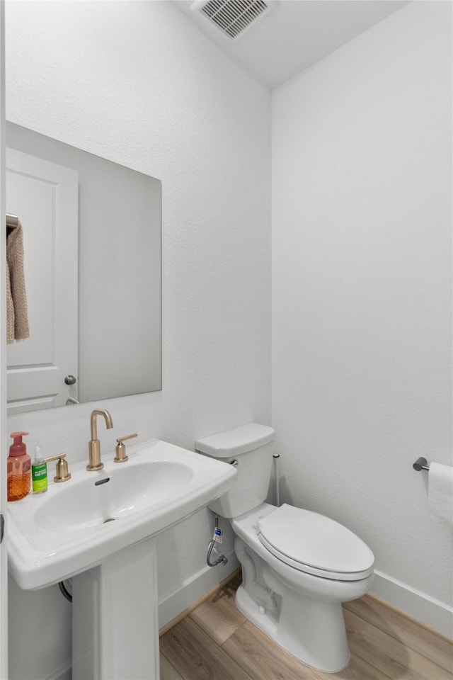 bathroom featuring toilet, wood finished floors, visible vents, and baseboards