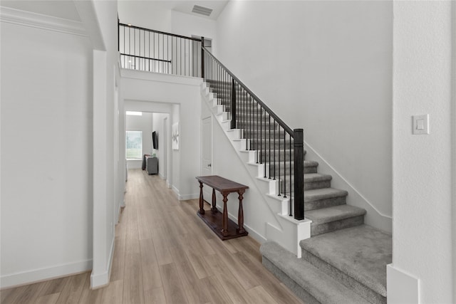 foyer entrance featuring light wood-style floors, baseboards, a high ceiling, and visible vents