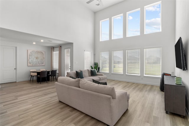 living area with a healthy amount of sunlight, light wood finished floors, baseboards, and a ceiling fan