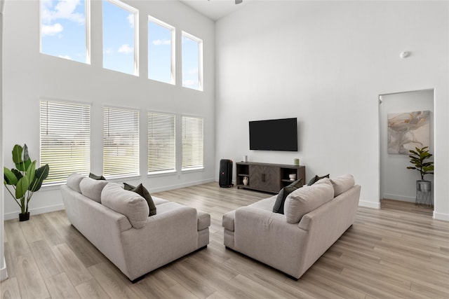 living area featuring baseboards, light wood-style flooring, and a towering ceiling