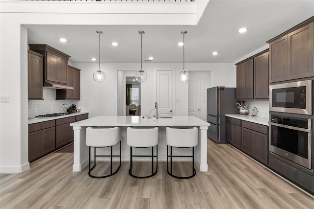 kitchen featuring a breakfast bar area, light wood-style flooring, light countertops, appliances with stainless steel finishes, and an island with sink