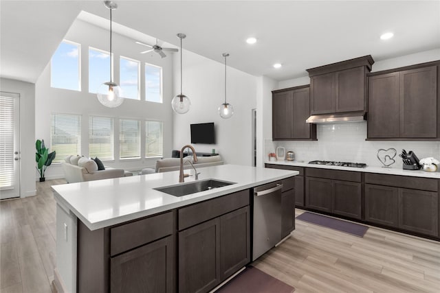 kitchen featuring light countertops, stainless steel dishwasher, open floor plan, a sink, and dark brown cabinets