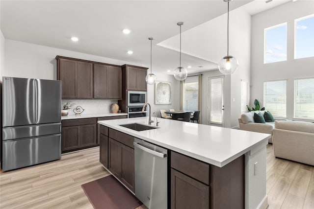 kitchen with dark brown cabinetry, light wood finished floors, light countertops, stainless steel appliances, and a sink