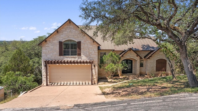 1017 Coventry Rd, Spicewood, TX 78669 - french country style house featuring stone siding, concrete driveway, an attached garage, and a standing seam roof