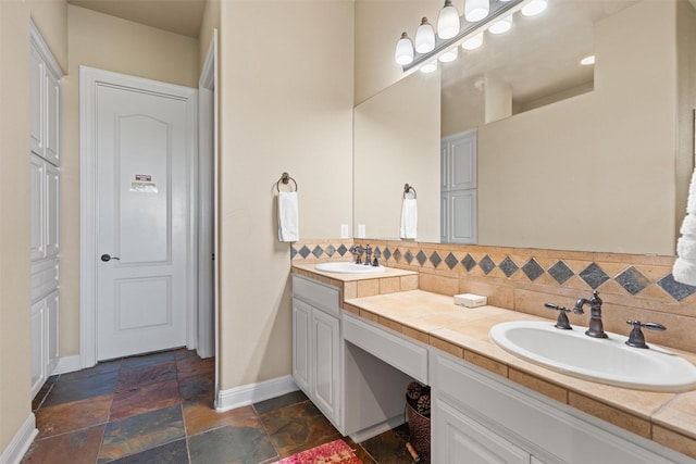 1017 Coventry Rd, Spicewood, TX 78669 - bathroom featuring baseboards, double vanity, decorative backsplash, and stone tile flooring