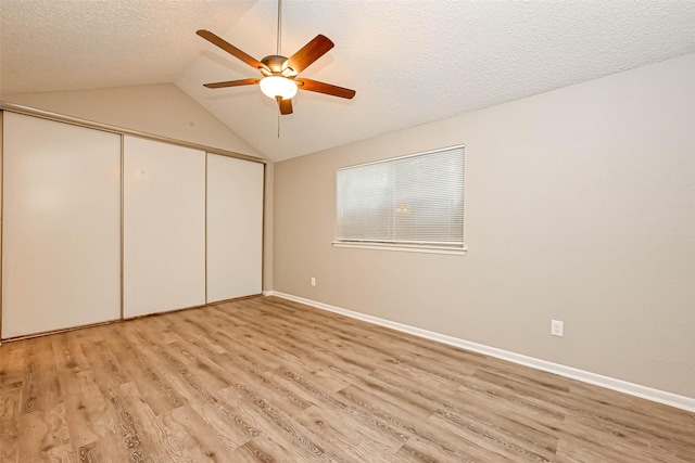 unfurnished bedroom with ceiling fan, a textured ceiling, vaulted ceiling, a closet, and light wood-type flooring