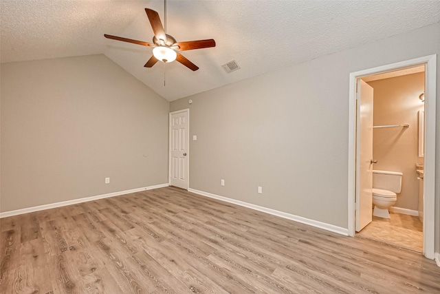 unfurnished bedroom featuring lofted ceiling, ensuite bath, ceiling fan, a textured ceiling, and light wood-type flooring