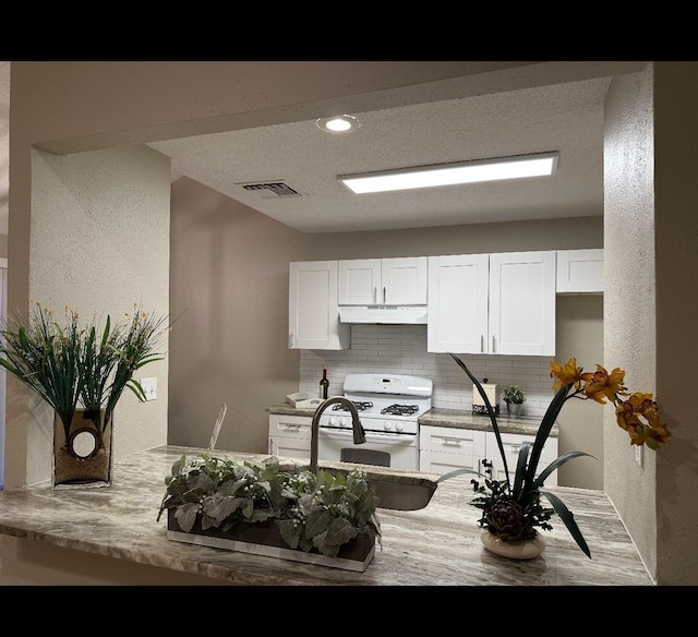 kitchen featuring light stone counters, white cabinets, white range with gas cooktop, decorative backsplash, and kitchen peninsula
