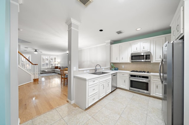 kitchen with decorative columns, stainless steel appliances, light countertops, white cabinetry, and a sink